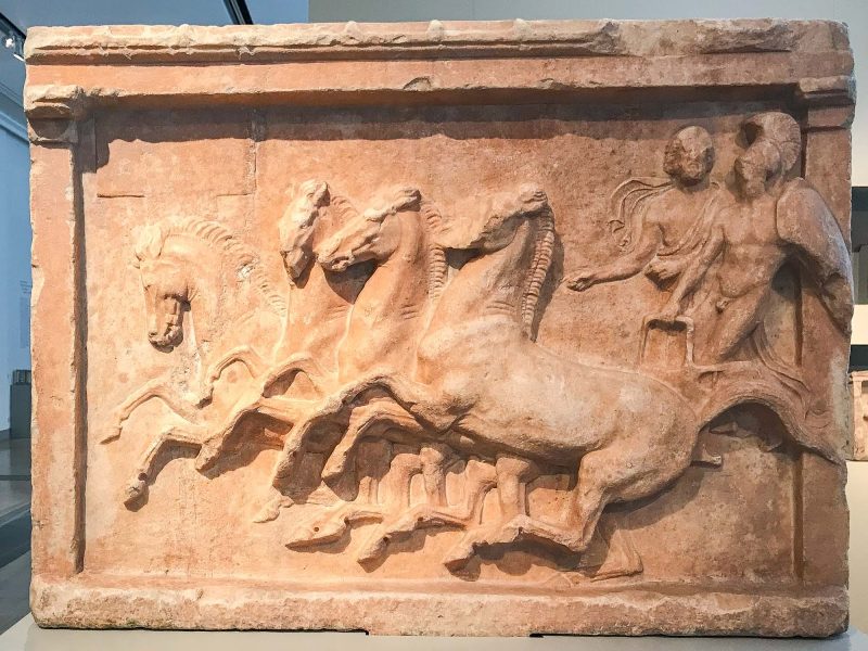 Votive relief for a chariot victory, a marble work from north of Athens, depicts a nude warrior wearing a helmet next to his bearded charioteer. Dates to 390-400 B.C. at the Altes Museum in Berlin.