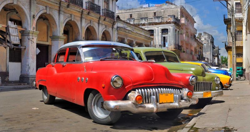Vintage cars line a street  in Cuba.