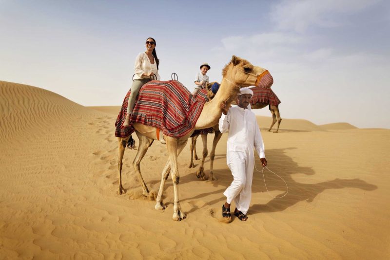 Hop on a camel with family members to explore the desert lands near Dubai.