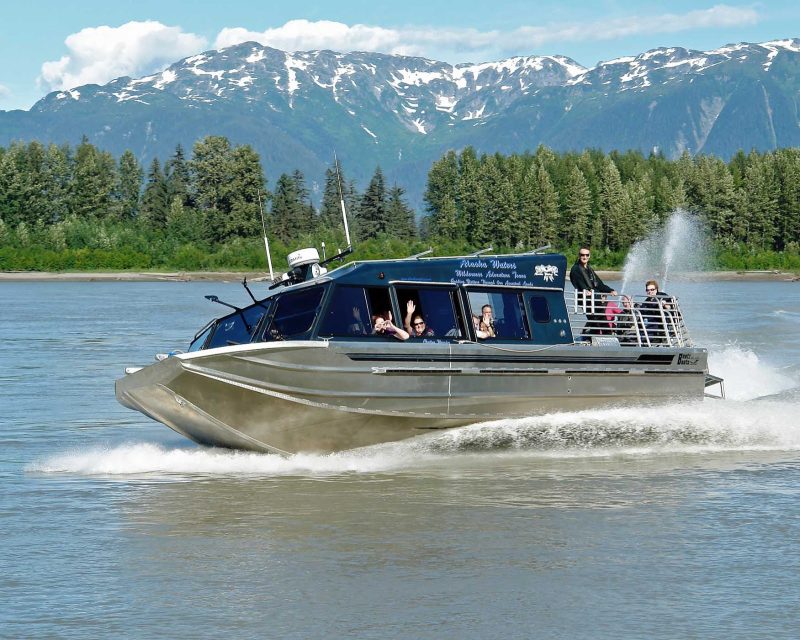 Explore the Stikine River in southeast Alaska on a jet boat ride, offering beautiful views of snow-capped mountains and lush riverbanks, during an American Cruise Lines voyage.