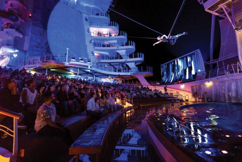 Audience members look up at a performer flying above water in the AquaTheater on Harmony of the Seas.