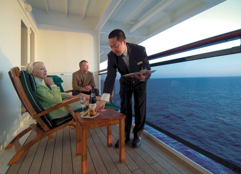 A butler serves guests on their private balcony in a Queens Grill suite (Q5) aboard Queen Mary 2.