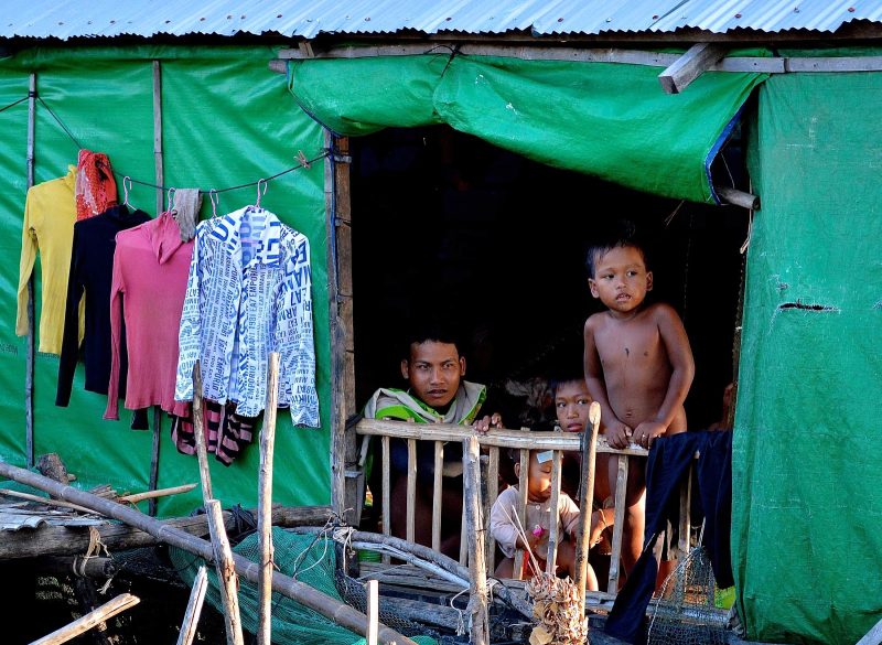 Family members peer out of a fairly typical house with green siding and tin roof in a rural part of Vietnam. 