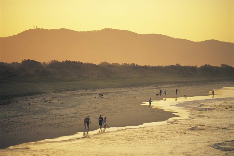 People stroll along the beach at sunset at Hat Head, near South West Rocks, Kempsey, North Coast, New South Wales, Australia.