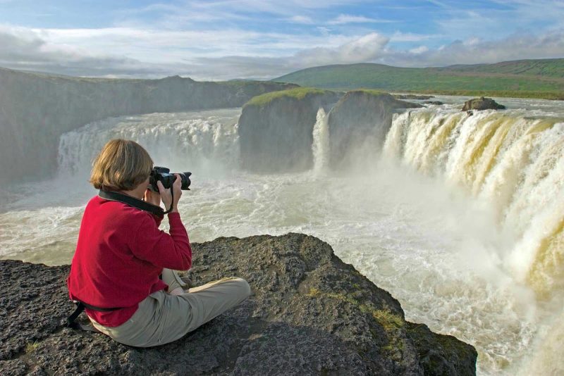 A traveler photographs the magnificent Godafoss (Waterfall of the Gods) on the Sktalfandafljot River during a Lindblad Expeditions tour of Iceland.