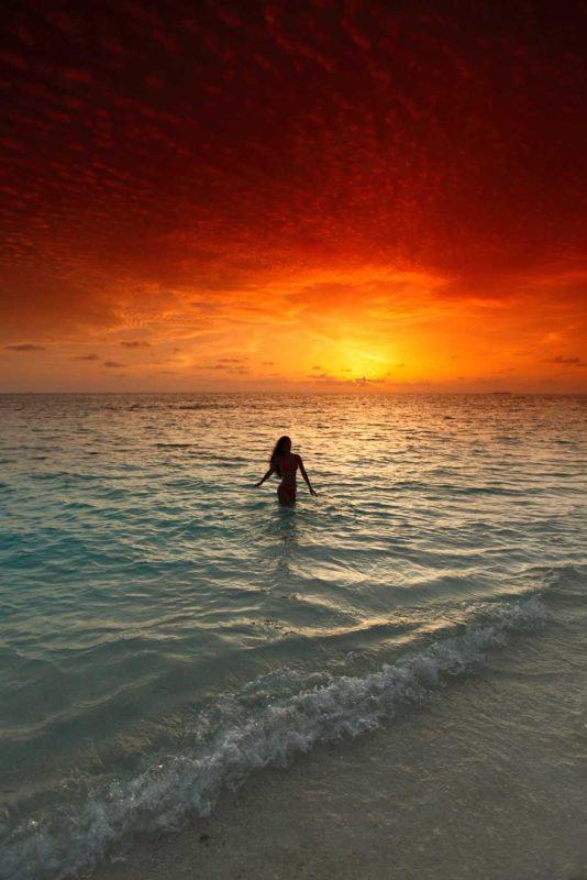 A Cuban woman wades in the surf at sunset.