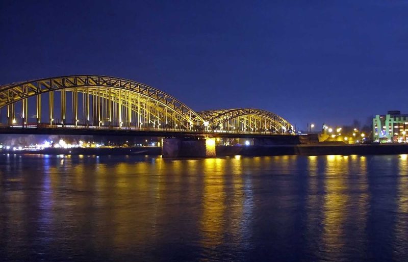 A view of the Railway Bridge spanning the Rhine River in Cologne, Germany, at night.