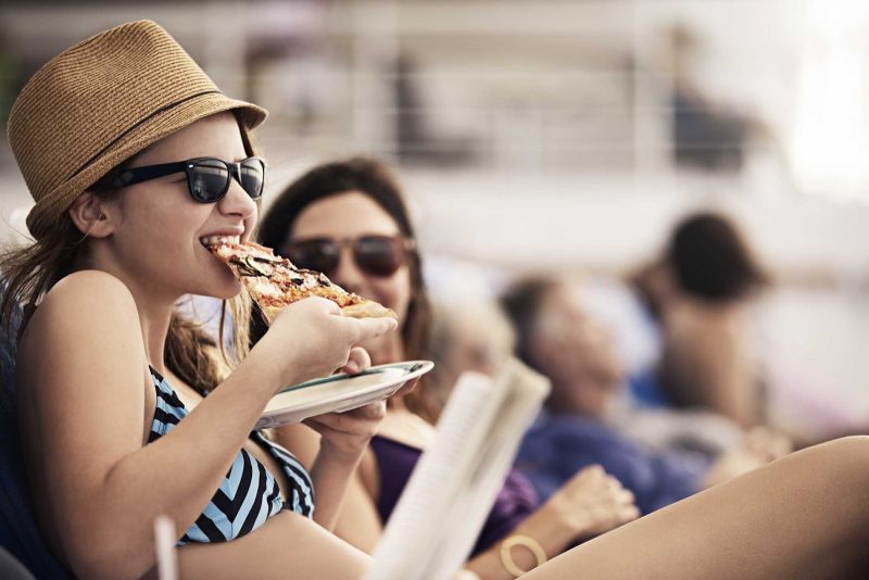 A young woman eats pizza on the deck of a Princess cruise.