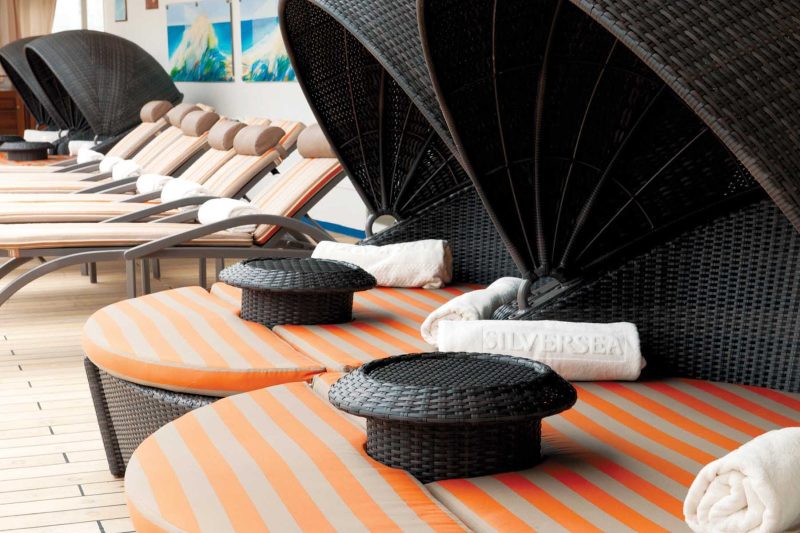 The pool deck on Silver Whisper features teak lounge chairs in the shade and sun, multiple bubbling whirlpools and a pool.