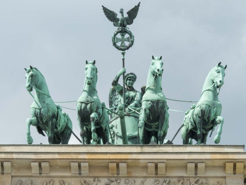 Brandenburg Gate is topped off with a statue known as the “Quadriga,” a statue of the goddess of victory driving a chariot pulled by four horses.