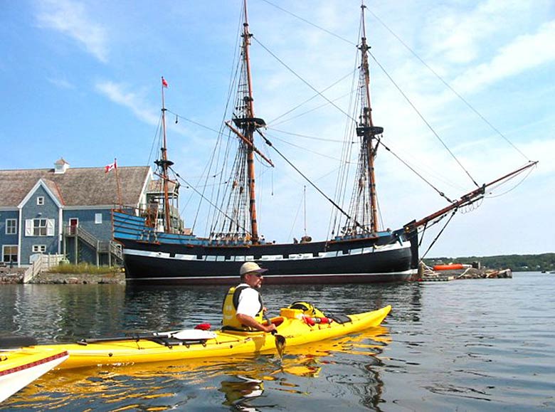 A kayaker heads out in front of the Hector, a replica that traces the region's Scottish heritage.