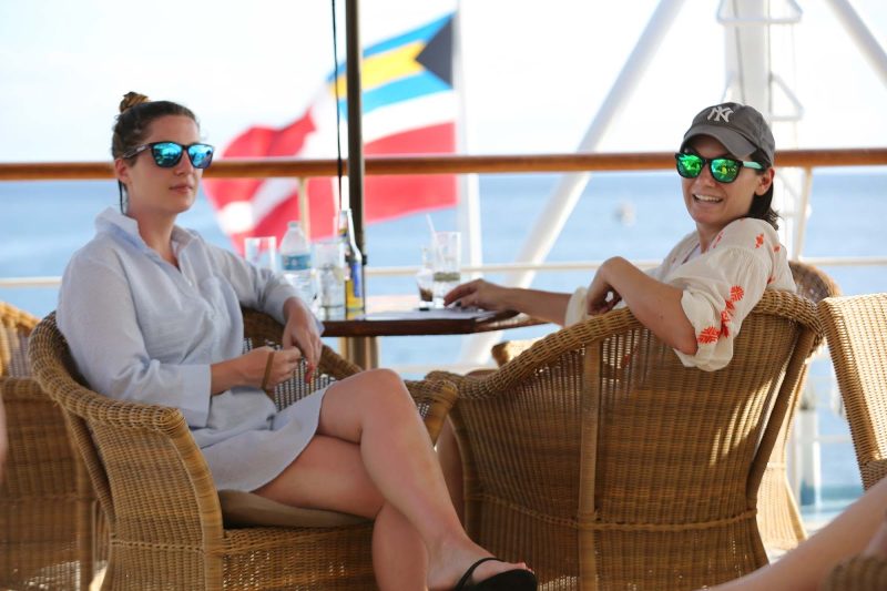 Two passengers from New York, with a flag wafting in the background, on the deck outside Compass Rose.