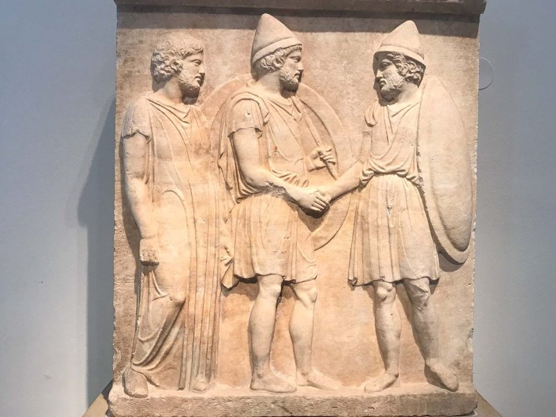 Funerary relief created at the end of the Peloponnesian War depicts two citizen soldiers from Athens armed with large round shields, lances and pilos helmets. It dates to 410 B.C. at the Altes Museum in Berlin.
