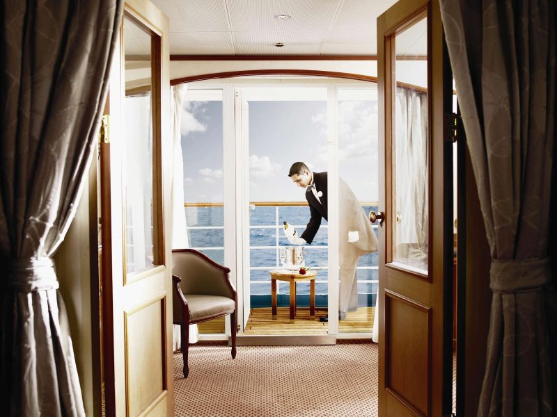 A butler on a Silversea sailing pours champagne on a guest's veranda.