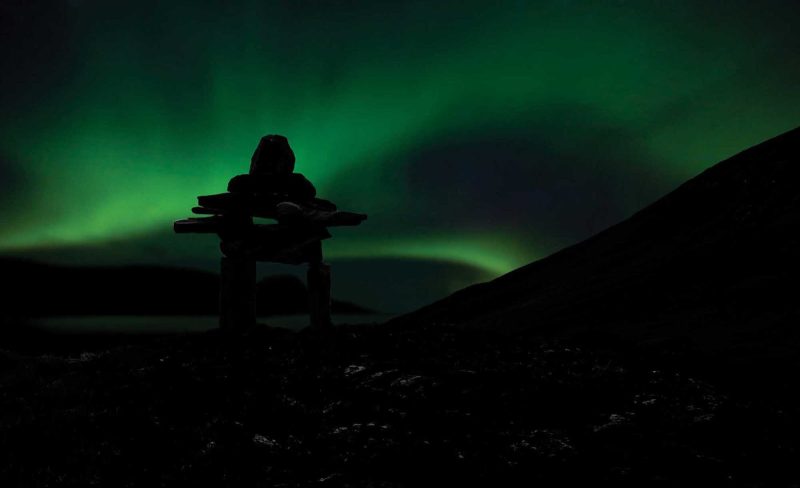 The Northern Lights seen against the silhouette of a rock edifice built by the native Inukshuk at Torngats Mountains in Newfoundland and Labrador Province.